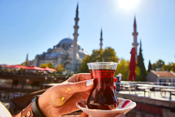A cup (armud) of traditional Turkish tea in hand against the background of a mosque in Istanbul