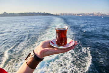 A cup (armud) of traditional Turkish tea  in hand against the background of the cityscape of Istanbul and the Sea of Marmara.