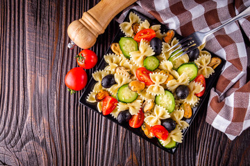 Delicious pasta salad with tomato cucumber and olives on wooden rustic background