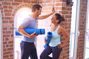 Fototapeta na wymiar Middle age beautiful sporty couple smiling happy. Standing with smile on face holding mat and speaking at gym