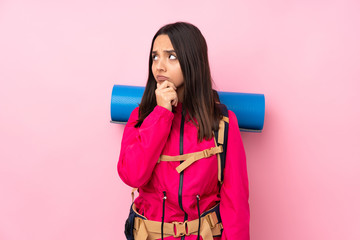 Young mountaineer girl with a big backpack over isolated pink background having doubts and with confuse face expression