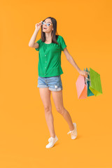 Beautiful young woman with shopping bags on color background