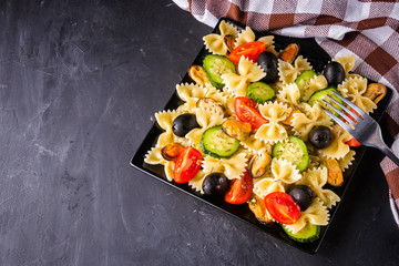 tasty pasta salad with tomato cucumber and olives on a dark stone background