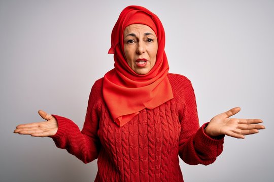 Middle age brunette woman wearing muslim traditional hijab over isolated white background clueless and confused with open arms, no idea concept.