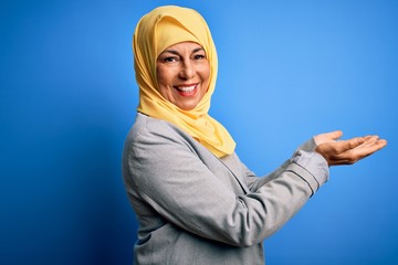 Middle age brunette business woman wearing muslim traditional hijab over blue background pointing aside with hands open palms showing copy space, presenting advertisement smiling excited happy