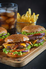 two burgers with fries and a drink on a dark background
