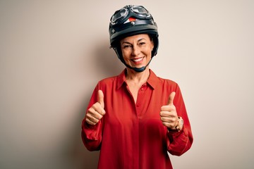 Middle age motorcyclist woman wearing motorcycle helmet over isolated white background success sign doing positive gesture with hand, thumbs up smiling and happy. Cheerful expression and winner