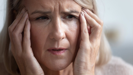 Close up head shot portrait unhealthy mature retired woman massaging temples, suffering from strong sudden headache. Unhappy middle aged woman having high blood pressure, healthcare concept.