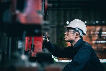 Men industrial engineer wearing a white helmet while standing in a heavy industrial factory behind....