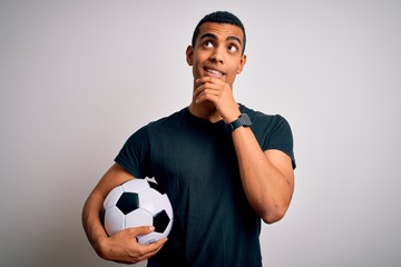 Handsome african american man playing footbal holding soccer ball over white background with hand on chin thinking about question, pensive expression. Smiling and thoughtful face. Doubt concept. © Krakenimages.com