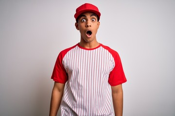 Young handsome african american sportsman wearing striped baseball t-shirt and cap afraid and shocked with surprise and amazed expression, fear and excited face.