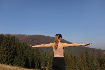 Young woman doing stretching exercises on nature in mountains. Sports girl practicing yoga pose in leggings. beautiful forest landscape