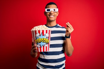 Young handsome african american man watching movie using 3d glasses eating popcorns with a happy and cool smile on face. Lucky person.