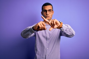 Handsome african american man wearing striped shirt and glasses over purple background Rejection expression crossing fingers doing negative sign