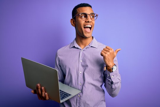 Young handsome african american business man working using laptop over purple background pointing and showing with thumb up to the side with happy face smiling