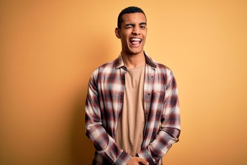 Young handsome african american man wearing casual shirt standing over yellow background winking looking at the camera with sexy expression, cheerful and happy face.