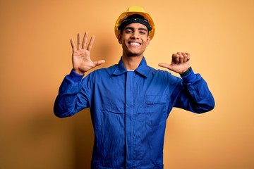 Young handsome african american worker man wearing blue uniform and security helmet showing and pointing up with fingers number six while smiling confident and happy.