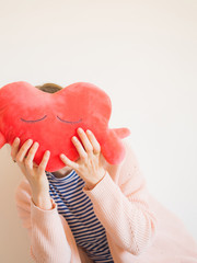 Faceless woman covering her face with red heart shaped plush toy.