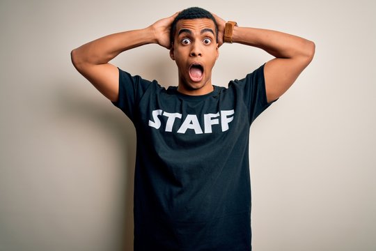 Young handsome african american worker man wearing staff uniform over white background Crazy and scared with hands on head, afraid and surprised of shock with open mouth