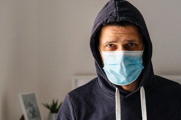 Portrait of caucasian adult man wearing protective medical mask and hood on his head to protect from virus bacteria pandemic pollution looking to the camera in day front view at home