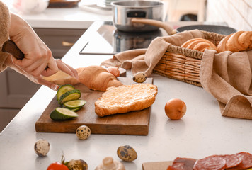 Woman preparing tasty croissant sandwich in kitchen, closeup