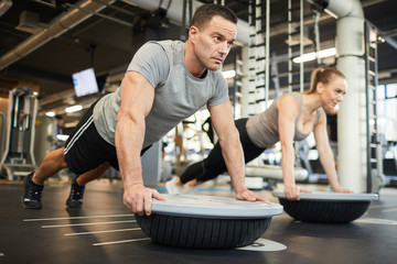 Full length portrait of mature muscular man doing balance exercises during couple workout in modern gym, copy space