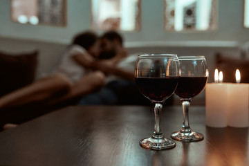 Romance never gets old. Wine glasses and candles on table with couple relaxing in the background on couch