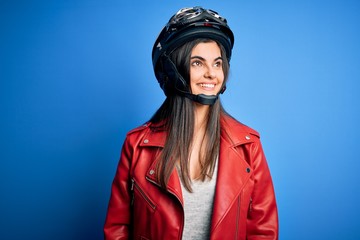 Young beautiful brunette motorcycliste woman wearing motorcycle helmet and jacket looking away to side with smile on face, natural expression. Laughing confident.