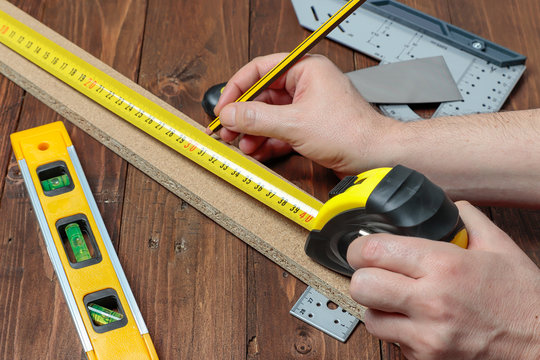hands using a flexometer to measure lenght of a wood strip on a space with others DIY tools