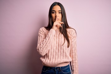 Young beautiful brunette woman wearing casual sweater over isolated pink background asking to be quiet with finger on lips. Silence and secret concept.