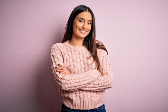 Young beautiful brunette woman wearing casual sweater over isolated pink background happy face smiling with crossed arms looking at the camera. Positive person.