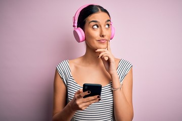 Young beautiful brunette woman listening to music using headphones and smartphone serious face...