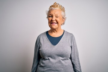 Senior beautiful grey-haired woman wearing golden queen crown over white background winking looking at the camera with sexy expression, cheerful and happy face.