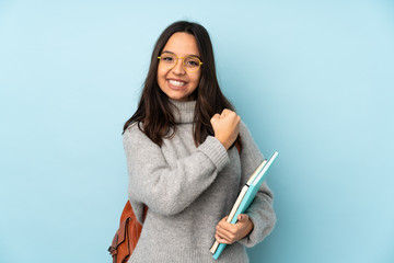 Young mixed race woman going to school isolated on blue background celebrating a victory