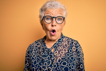 Senior beautiful grey-haired woman wearing casual shirt and glasses over yellow background afraid...