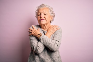 Senior beautiful woman wearing casual t-shirt standing over isolated pink background Hugging oneself happy and positive, smiling confident. Self love and self care