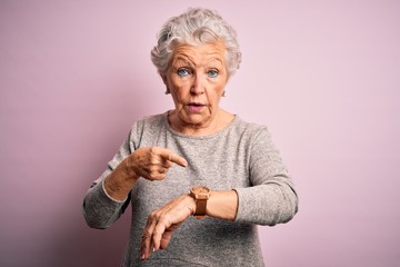 Senior beautiful woman wearing casual t-shirt standing over isolated pink background In hurry pointing to watch time, impatience, upset and angry for deadline delay