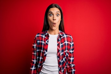 Fototapeta premium Young beautiful brunette woman wearing casual shirt standing over isolated red background afraid and shocked with surprise expression, fear and excited face.