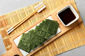 Tasty seaweed sheets with soy sauce and chopsticks on bamboo mat