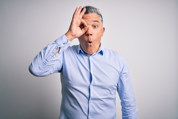 Middle age handsome grey-haired business man wearing elegant shirt over white background doing ok gesture shocked with surprised face, eye looking through fingers. Unbelieving expression.