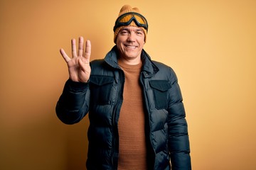Middle age handsome grey-haired skier man on vacation wearing ski goggles showing and pointing up with fingers number four while smiling confident and happy.