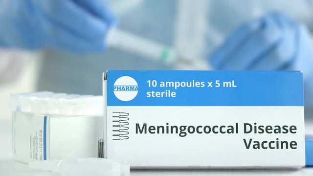 Ampoules with meningococcal disease vaccine on the table near working laboratory assistant, fictional logo on the box