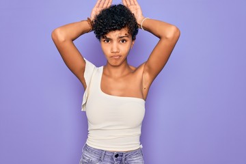 Young beautiful african american afro woman wearing casual t-shirt over purple background Doing bunny ears gesture with hands palms looking cynical and skeptical. Easter rabbit concept.