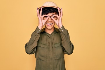 Young beautiful african american tourist woman wearing glasses and explorer hat doing ok gesture like binoculars sticking tongue out, eyes looking through fingers. Crazy expression.