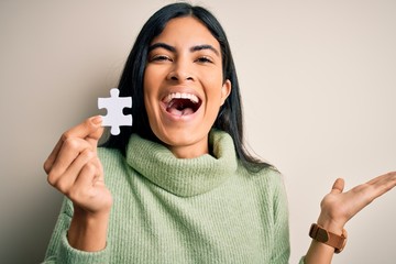 Young beautiful hispanic woman holding puzzle piece as cooperation solution on business very happy...