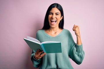 Young beautiful hispanic student woman reading a book over pink isolated background screaming proud and celebrating victory and success very excited, cheering emotion