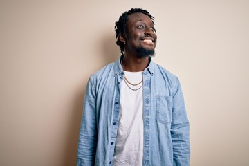 Obraz premium Young handsome african american man wearing casual denim shirt over white background looking away to side with smile on face, natural expression. Laughing confident.