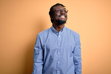 Obraz premium Young handsome african american man wearing shirt and glasses over yellow background looking away to side with smile on face, natural expression. Laughing confident.
