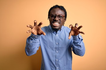 Young handsome african american man wearing shirt and glasses over yellow background smiling funny...