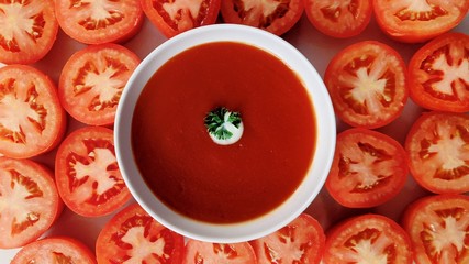 Tomato soup in ceramic bowl surrounded by sliced tomato on marble surface